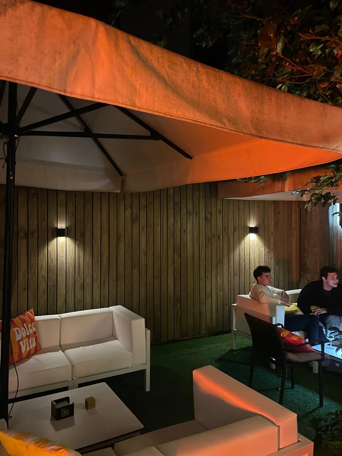 Dos personas charlando en los sofás de la terraza de noche, bajo las sombrillas iluminadas en tono cálido