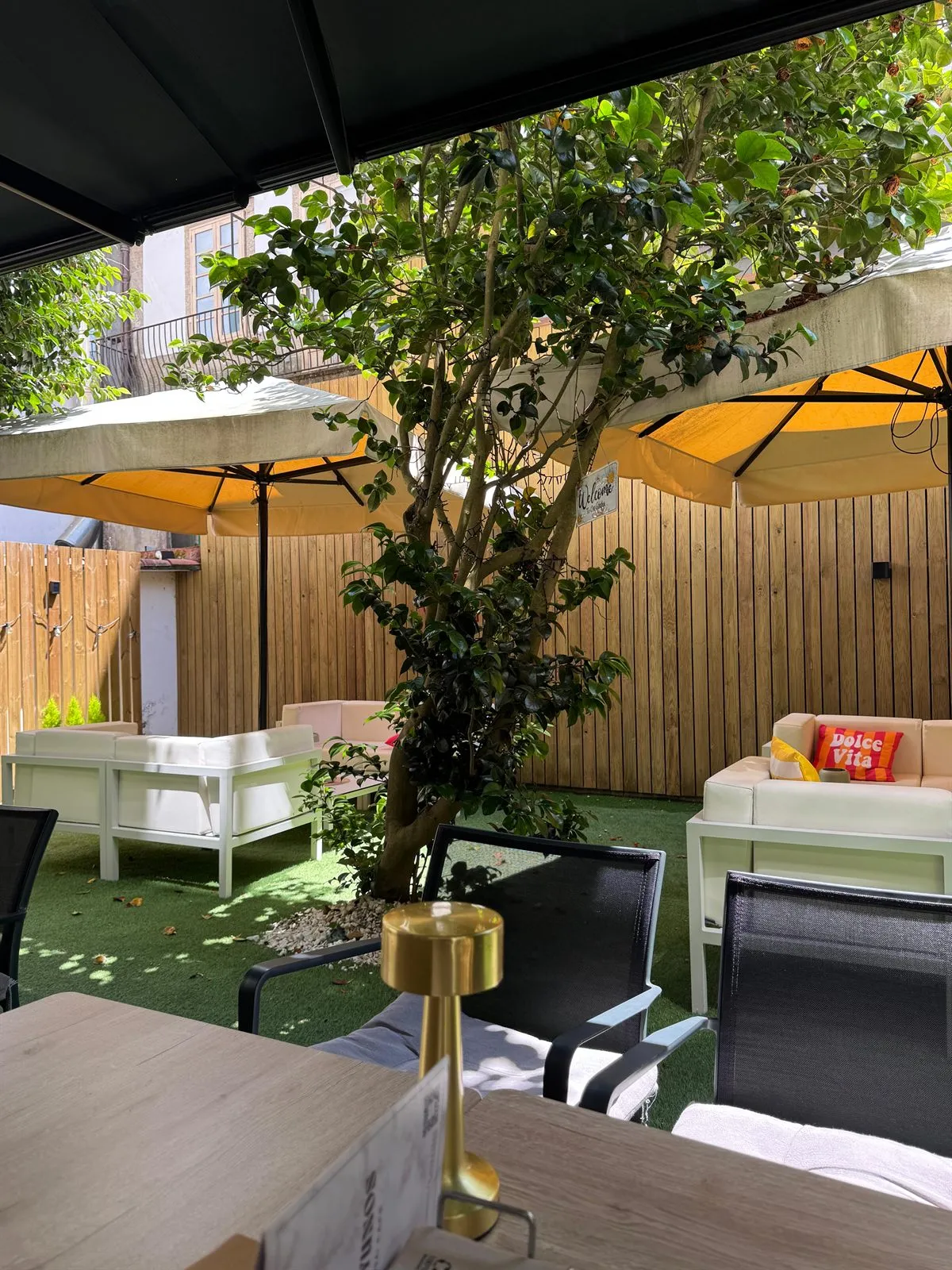 Zona chill-out de la terraza a mediodía, con sofás blancos, sombrillas y la camelia dando sombra