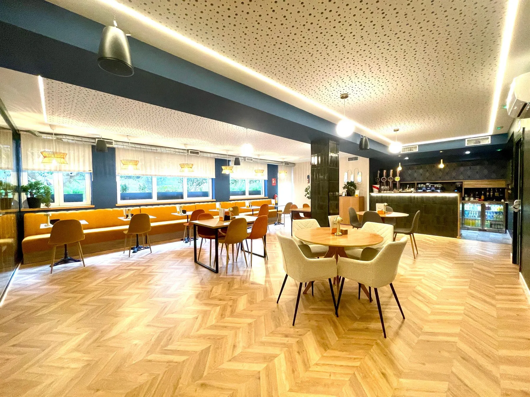 Sala interior de Bonsai Café, con suelo de espiga, banco corrido amarillo bajo los ventanales y la barra al fondo