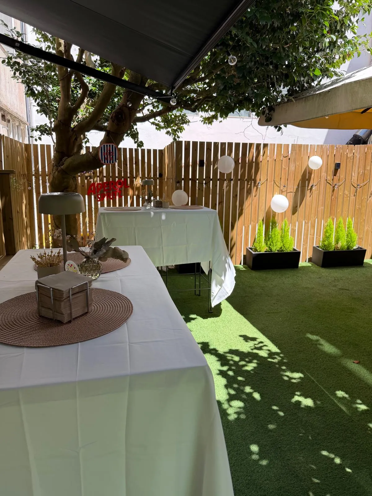 Terraza de Bonsai Café con dos mesas largas vestidas de blanco, guirnalda de luces y la camelia dando sombra